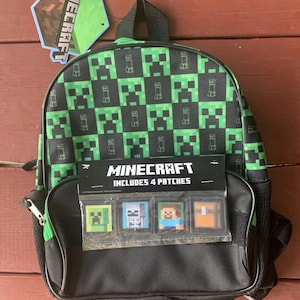 May include: A black and green Minecraft backpack with a green and black checkered pattern. The backpack has a zipper closure and a small pocket on the front. The front pocket has a clear plastic window that shows four Minecraft character patches. The text "Minecraft Includes 4 Patches" is printed on the front pocket.