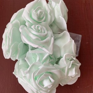 May include: A bunch of pale green artificial roses. The roses have multiple layers of petals and are arranged in a compact bunch. The color is a soft, pastel green, and the roses appear to be made of a soft material.