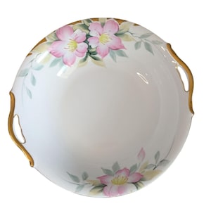 Puede incluir: Bol de porcelana blanca con detalles florales rosas y hojas verdes. El borde está adornado con pintura dorada y el cuenco tiene dos asas doradas. Las flores tienen centros amarillos.