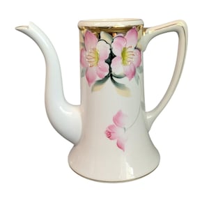 Może przedstawiać: Biały porcelanowy dzbanek do kawy z długim dziobkiem i uchwytem. Dzbanek jest ozdobiony różowymi wzorami kwiatowymi i złotymi obramowaniami na górze. Kwiaty mają żółte środki i zielone liście.