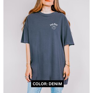 May include: An oversized t-shirt in a denim blue colour with the text "leg day" and a smiley face graphic.