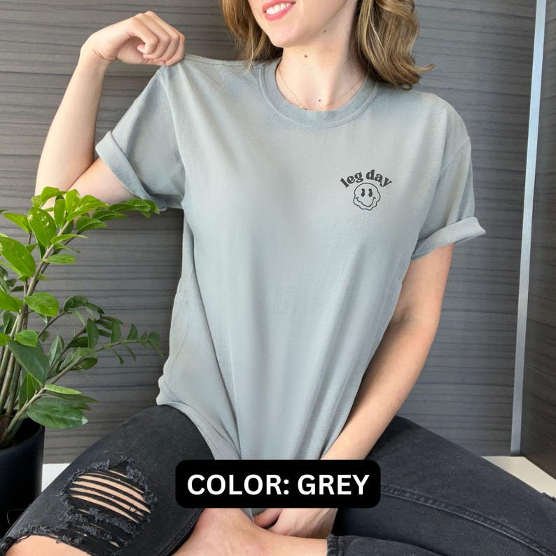 May include: A grey t-shirt with a black smiley face and the text "leg day" printed on the front.