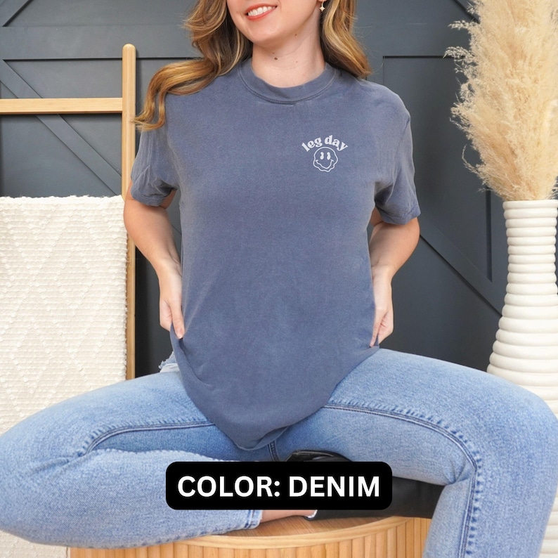 May include: A denim blue t-shirt with the text "leg day" and a smiley face graphic.