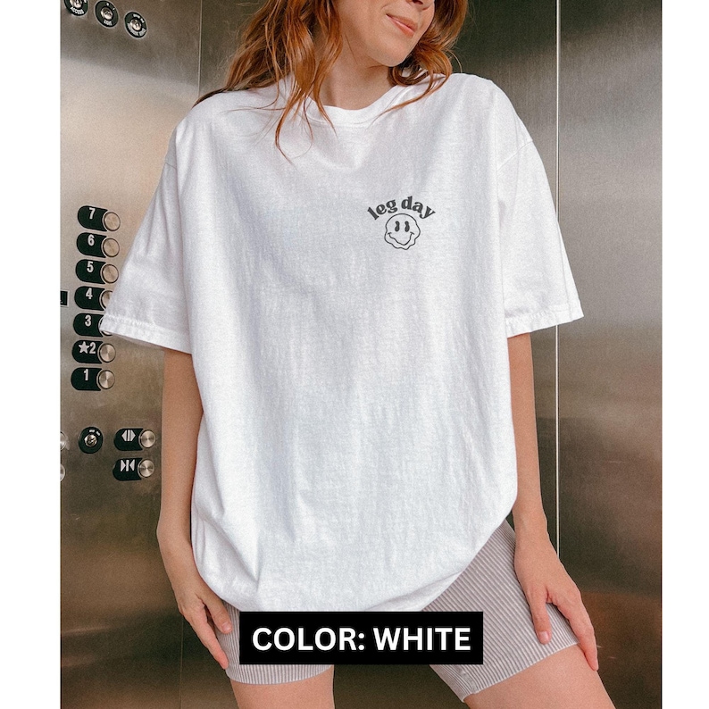 May include: White oversized t-shirt with a black smiley face graphic and the text "leg day" on the front.