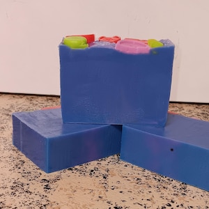 May include: Three bars of blue soap with colorful decorative swirls on top. The soap is handmade and has a natural, earthy scent.