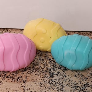May include: Three plastic Easter eggs in different colors: pink, yellow, and blue. Each egg has a wavy pattern.