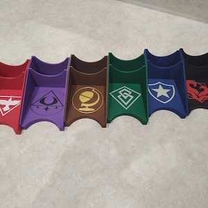 May include: A set of seven multi-colored card holders. Each holder is a different color, including red, purple, brown, green, blue, and black. Each holder has a unique white or gold graphic design on the front, such as a bird, a crescent moon, or a globe.