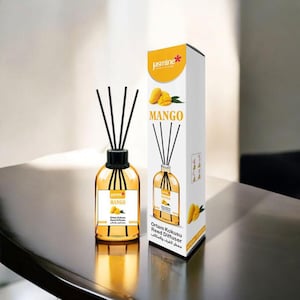 May include: A clear glass bottle with black reeds and a yellow label that says "Mango" and "Ortam Kokusu Reed Diffuser". The bottle is sitting on a wooden table next to a white box with a yellow mango on it. The box also says "Mango" and "Ortam Kokusu Reed Diffuser".