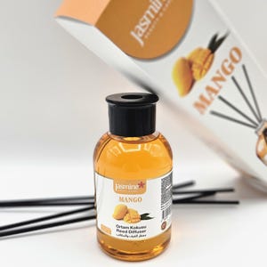 May include: A mango-scented reed diffuser with a clear glass bottle and black cap. The bottle contains a golden-colored liquid and is labeled "Mango" with the brand name "Jasmine". The packaging includes a box with mango illustrations and the word "Mango".