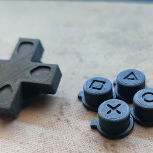 May include: A set of black gaming controller replacement parts including a cross-shaped directional pad and four circular action buttons featuring embossed square, triangle, cross, and circle symbols on their top surfaces.