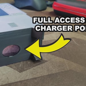 Puede incluir: Primer plano de un dispositivo electr&oacute;nico gris y blanco con el texto "FULL ACCESS TO CHARGER PORT" y una flecha amarilla que apunta a una abertura circular. El dispositivo est&aacute; sobre una superficie estampada.
