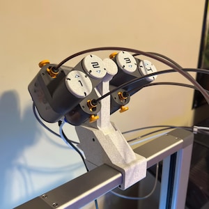 May include: A gray and black robotic device with four numbered cylinders and yellow accents. The cylinders are labeled 1, 2, 3, and 4. Black tubes and wires extend from the device, which is mounted on a gray frame.