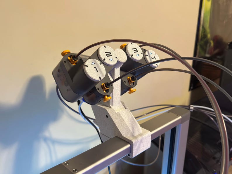 May include: A gray and black robotic device with four numbered cylinders and yellow accents. The cylinders are labeled 1, 2, 3, and 4. Black tubes and wires extend from the device, which is mounted on a gray frame.