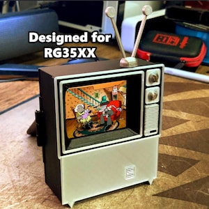 May include: A miniature retro-style television with a black and white frame and a screen displaying a cartoon scene. The TV has silver antenna and knobs, and the text "Designed for RG35XX" is visible on the top.
