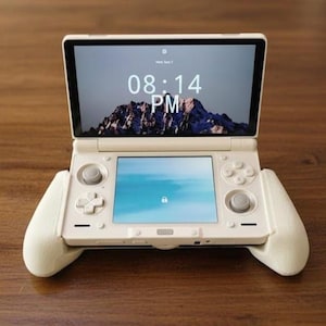 May include: A white handheld gaming console with a screen displaying a mountain landscape and the time 08:14 PM. The console has a lower screen, buttons, and attached white grips for comfortable handling.