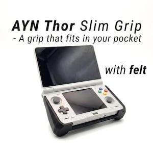 May include: A white handheld gaming console with a black screen and colorful buttons, secured in a black slim grip accessory. The text reads: AYN Thor Slim Grip - A grip that fits in your pocket with felt. The device features a D-pad and dual joysticks.