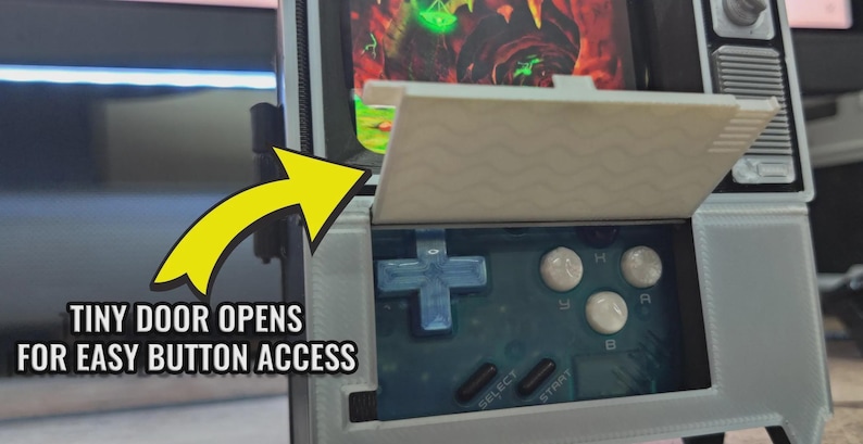 Puede incluir: Una consola de juegos port&aacute;til con un dise&ntilde;o de televisor retro. La pantalla muestra un videojuego, y el dispositivo tiene botones y una cruceta. El texto "TINY DOOR OPENS FOR EASY BUTTON ACCESS" es visible.