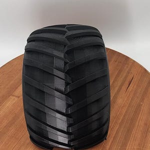 Puede incluir: Un neum&aacute;tico negro de tractor con un dibujo profundo en la banda de rodadura. El neum&aacute;tico es cil&iacute;ndrico y parece estar hecho de un material duro y duradero. El neum&aacute;tico est&aacute; sobre una superficie de madera.