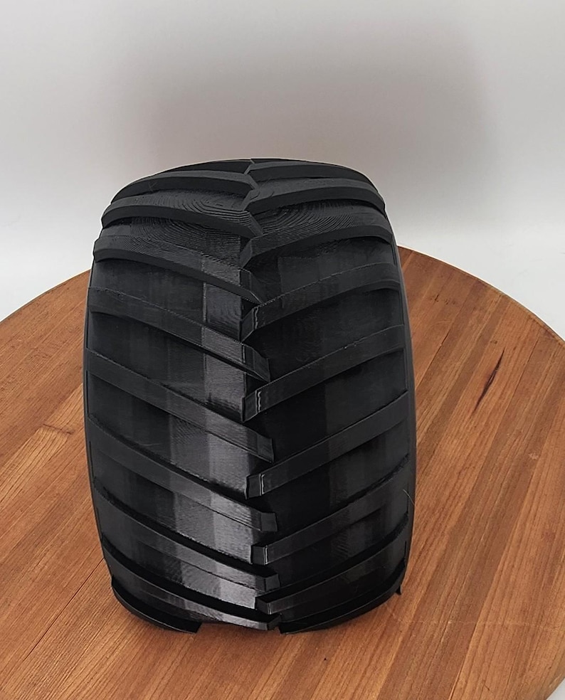 Puede incluir: Un neum&aacute;tico negro de tractor con un dibujo profundo en la banda de rodadura. El neum&aacute;tico es cil&iacute;ndrico y parece estar hecho de un material duro y duradero. El neum&aacute;tico est&aacute; sobre una superficie de madera.