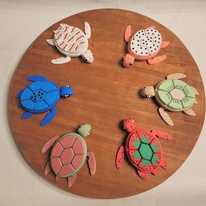 May include: Six colorful turtle figurines on a wooden surface. The turtles are painted in various colors and patterns, including blue, green, red, and white.