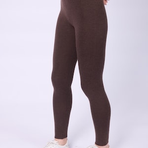 May include: Brown leggings. The leggings are a solid, dark brown color and appear to be made of a soft, stretchy material. The leggings are ankle-length and are paired with white sneakers.