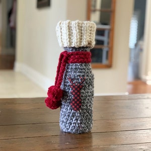 May include: A grey and white crocheted bottle cosy with a red pom-pom and a red and black plaid reindeer design.