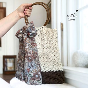 May include: A crocheted tote bag with brown wooden handles. The bag is white with a brown crocheted bottom and has a paisley patterned scarf tied around the handles.