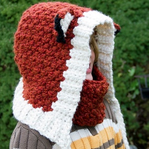 May include: A red and white crocheted fox hat with a white crocheted scarf. The hat has a pointed hood and a fox face with black ears.