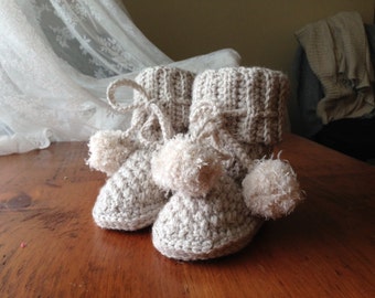 Pode incluir: Um par de pantufas de crochê bege com pompons fofinhos.