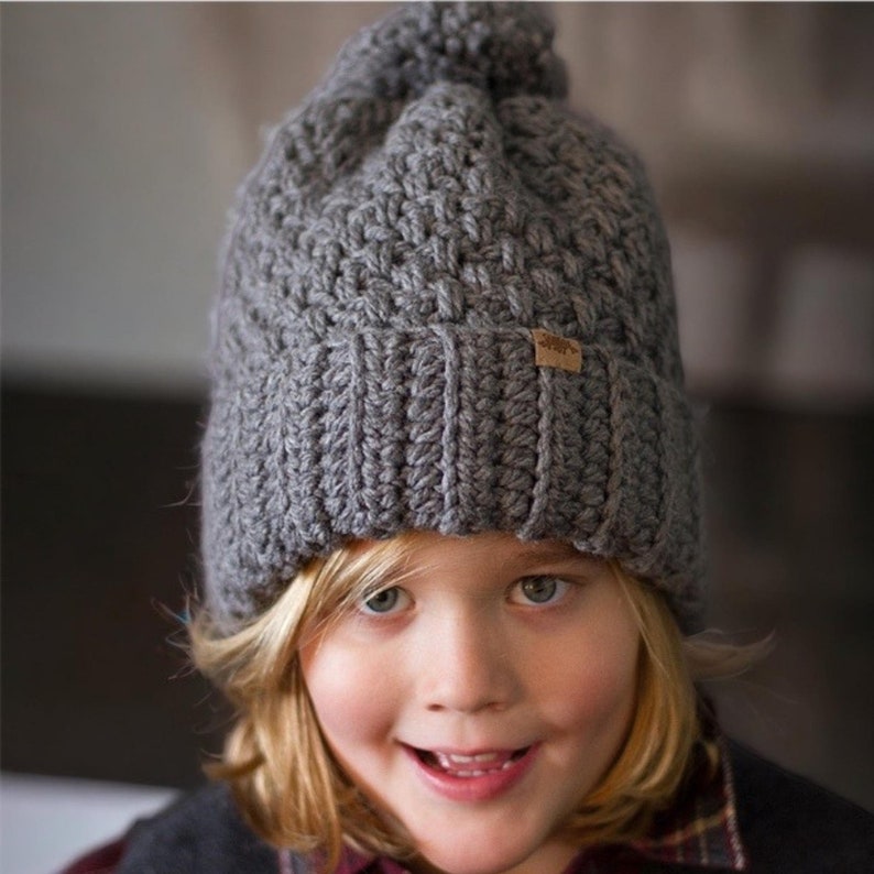 a child wearing a grey thick crochet hat with a rolled brim and knit look texture with pompom
