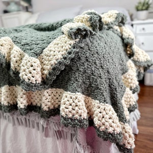 a green crocheted blanket  with cream crochet border sits on a bed