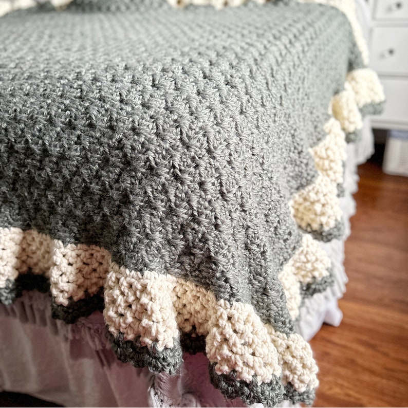 a green crocheted blanket  with cream crochet border sits on a bed