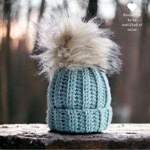 A crochet ribbed beanie hat in soft aqua colour blurred out forest in the background