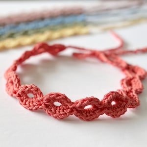 Può includere: Un cerchietto in crochet rosa corallo con un delicato design a scalare.