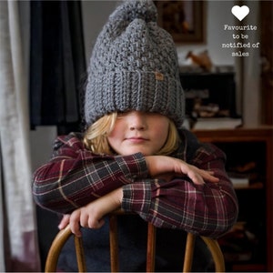 a child wearing a grey thick crochet hat with a rolled brim and knit look texture with pompom