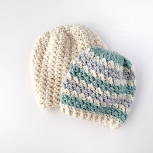 Puede incluir: Dos gorros de ganchillo, uno de color crema sólido y el otro con rayas de crema, gris y verde claro.