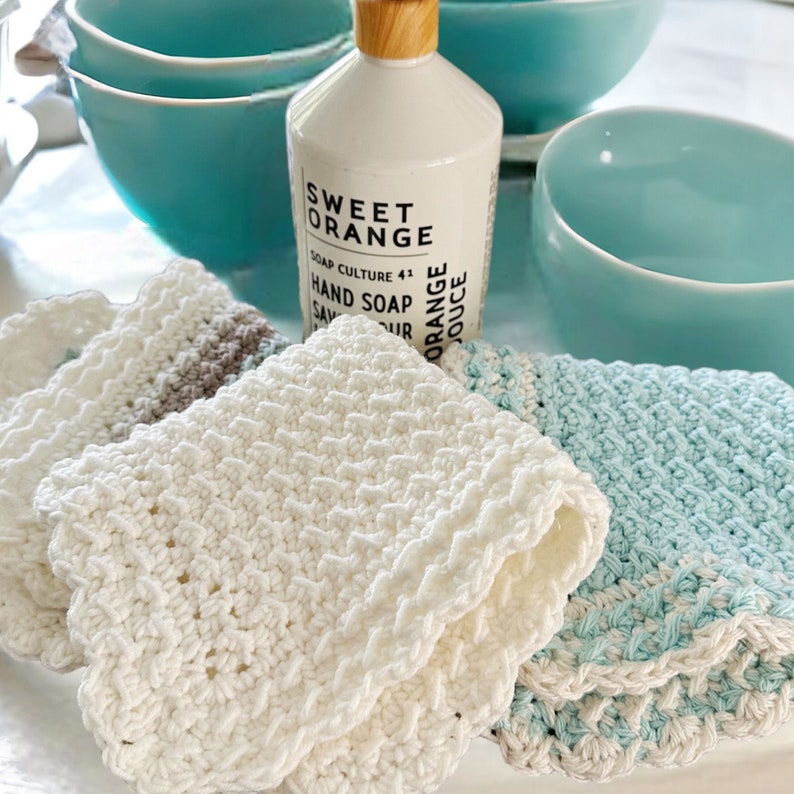three crochet dishcloths made using the crochet crunch stitch clothes are in aqua cream and brown with a contrast border