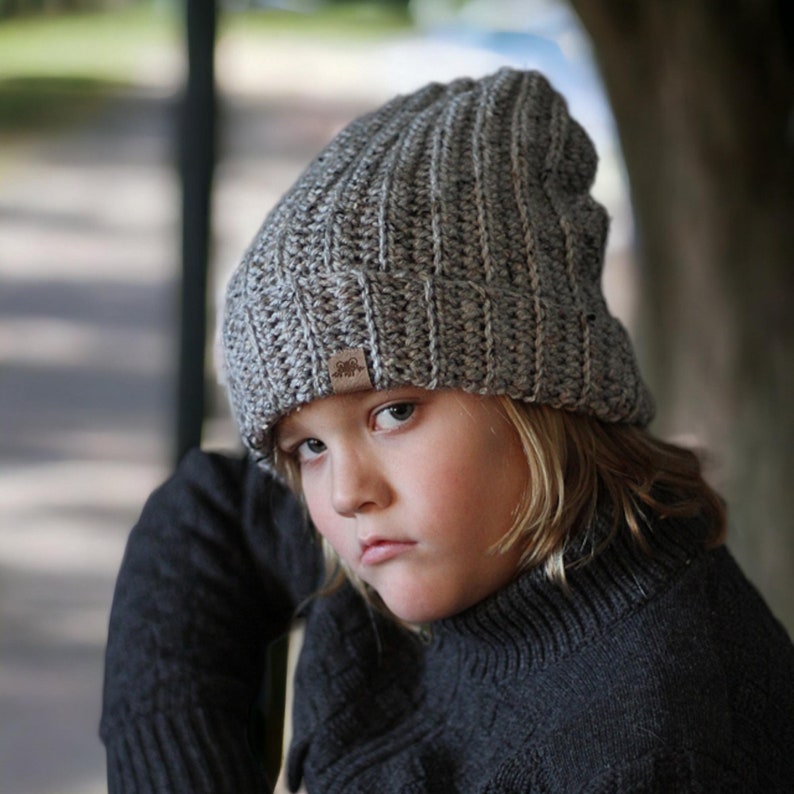 boy wearing a crochet ribbed beanie in grey with a forest in the background