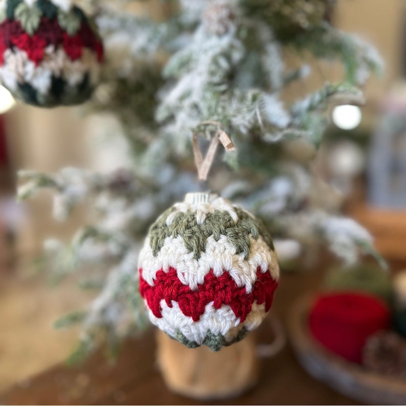 May include: Crocheted Christmas ornaments in red, white, and green. The handmade ornaments are hanging on a snow-covered Christmas tree. The ornaments have a textured, zig-zag pattern.