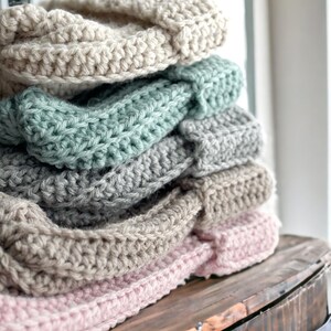 stack of crochet ribbed beanies in cream grey beige and pink a different size on a wood dresser