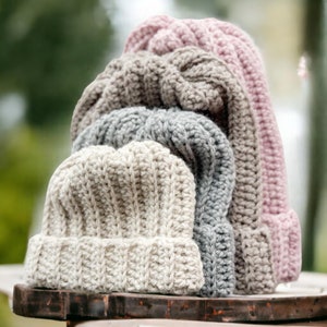 stack of crochet ribbed beanies in cream grey beige and pink a different size forest in the background