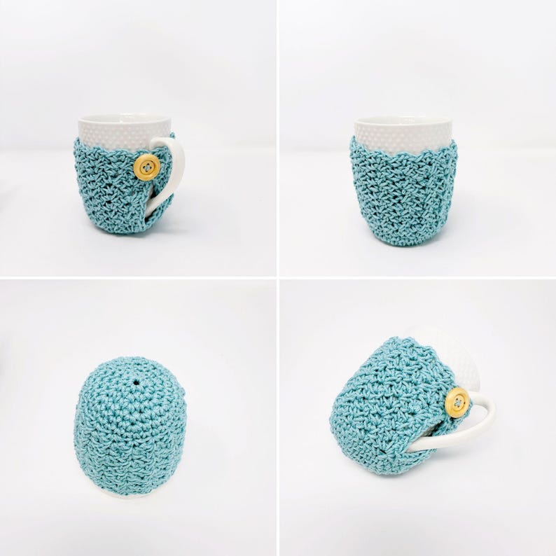May include: A white ceramic mug with a light blue crocheted cozy. The cozy is secured with a wooden button. The mug has a white handle and a dotted pattern. The cozy is a textured, handmade item.