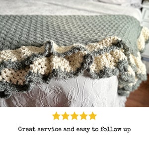 a green crocheted blanket  with cream crochet border sits on a bed