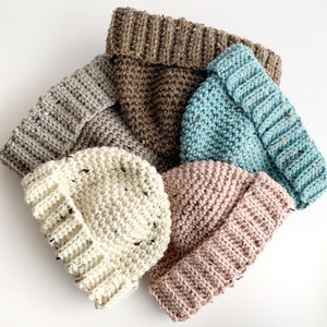 May include: Five crocheted hats in different colours and textures. The hats are beige, brown, light blue, pink, and white.
