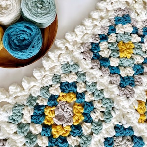 May include: A crocheted blanket with a geometric pattern in shades of white, teal, gray, and yellow.