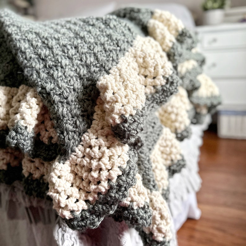 a green crocheted blanket  with cream crochet border sits on a bed