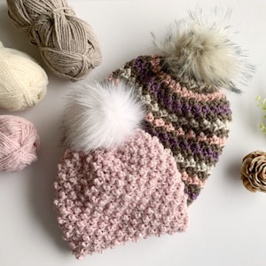Puede incluir: Dos gorros de ganchillo con pompones de piel sintética. Un gorro es rosa y el otro tiene un patrón de rayas multicolores.