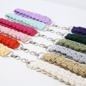 May include: A collection of colorful crochet wrist straps with silver-tone swivel clasps. The straps are in various colors, including purple, blue, pink, orange, and cream. The crochet stitch creates a textured appearance. These wrist straps are ideal for keys or small accessories.