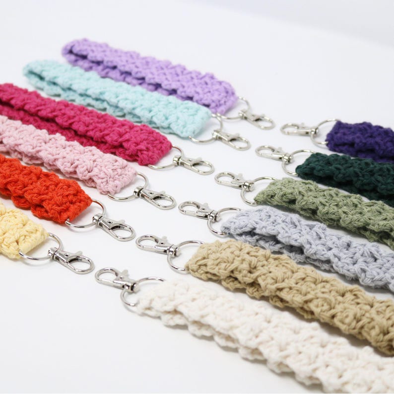 May include: A collection of colorful crochet wrist straps with silver-tone swivel clasps. The straps are in various colors, including purple, blue, pink, orange, and cream. The crochet stitch creates a textured appearance. These wrist straps are ideal for keys or small accessories.