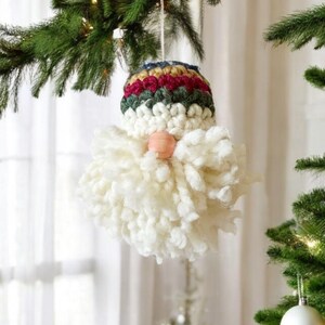 May include: A white yarn gnome ornament with a striped hat in shades of red, green, blue, and gold. The gnome has a wooden nose and a white yarn beard.